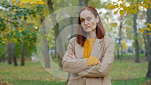 Serious offended Caucasian woman in autumn park in city outdoors posing confident alone looking at camera angry sad