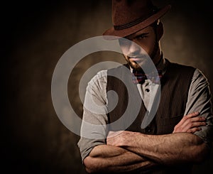 Serious old-fashioned man with hat posing on dark background.