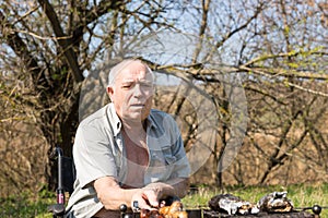 Serious Old Man Roasting Sausage at Camp Area