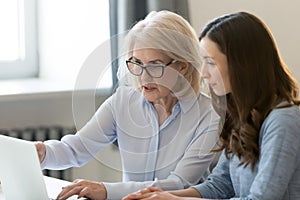 Serious old mentor teaching intern or student pointing at laptop