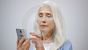 Serious old woman looking cellphone indoors. Senior lady searching news inside.