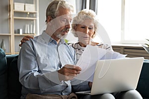 Serious older couple managing budget together, reading documents