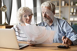 Serious older couple reading financial documents, planning budget