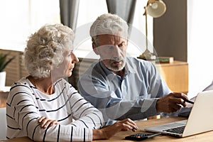 Serious older couple using laptop, planning budget, checking bills