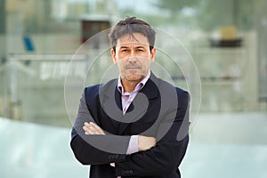 Serious older man in business suit standing with arms crossed outdoors