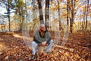 Serious older man sitting on stump in woods