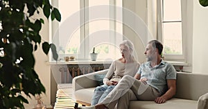 Serious older spouses sit on sofa talking looking troubled