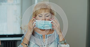 Serious older woman putting surgical mask that protects from epidemic outbreak. Senior woman looking to camera portrait