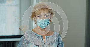 Serious older woman putting surgical mask that protects from epidemic outbreak. Senior woman looking to camera portrait