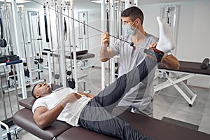 Serious patient doing straight leg raise using gym equipment