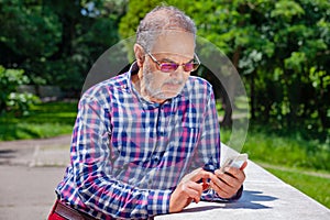 Serious Pensioner with Casual Clothing Glasses and Phone in Park