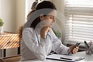 Serious pensive female general practitioner using app on smartphone