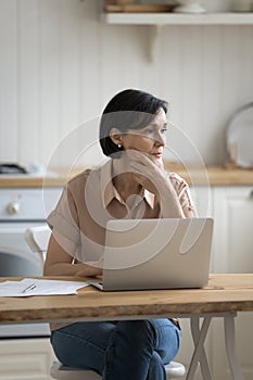 Vážny zamyslený zrelý žena sedieť na kuchyňa stôl prenosný počítač 