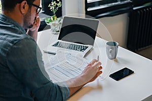 Serious pensive thoughtful focused young casual businessman or entrepreneur in office filling income tax return papers documents