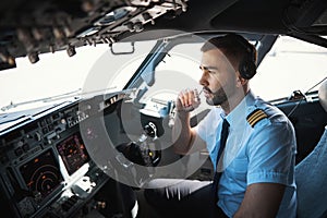 Serious pilot talking to the coworkers in the microphone