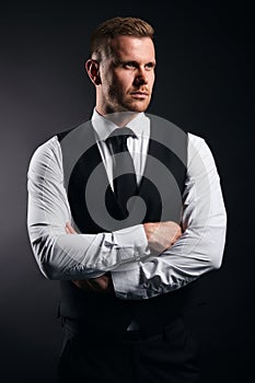 Serious pleasant strong man in fashion shirt, vest and tie crossing his arms