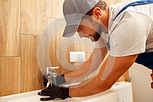 Serious plumber, male worker in uniform installing tap or bathroom faucet