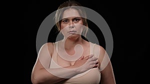 Serious plus size woman putting hand on chest raising palm swearing at black background. Portrait of Caucasian obese