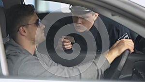 Serious policeman checking male drivers license after exceeding speed limit