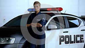 Serious policewoman in uniform leaning on patrol car, maintenance of order