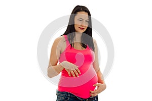 Serious pregnant future mother in pink shirt touching her belly isolated on white background