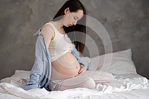 serious pregnant woman touching her beautiful belly sitting in the bed. Pregnancy, motherhood and expectation