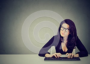 Serious preoccupied young woman sitting at desk typing on keyboard of a desktop