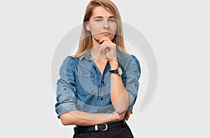 Serious pretty blonde young woman wearing denim shirt with finger folded on the chin frowning her face and looking to the camera