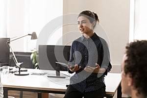 Serious pretty young Indian businesswoman leader talking to team