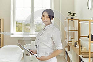 Serious professional beautician standing in her beauty salon and looking at camera