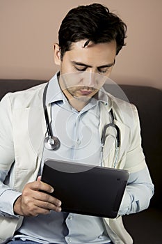 Serious professional doctor in white coat and stethoscope holding modern touch screen gadget using digital tablet computer at work