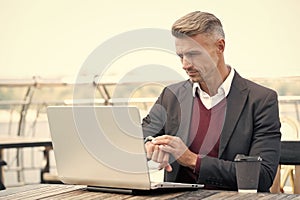Serious professional man check time on watch working on laptop computer outside, punctuality