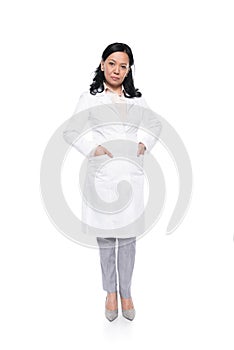 Serious professional medical worker in white coat standing with hands in pockets