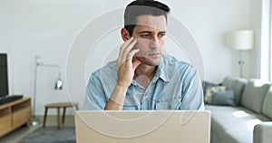 Serious puzzled Hispanic man sit at desk working on laptop