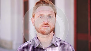 Serious Redhead Man Looking at Camera standing outdoors. Close Up Portrait of sad young guy.