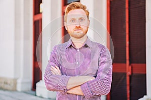 Serious Redhead Man Looking at Camera standing outdoors. Close Up Portrait of sad young guy.