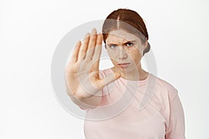 Serious redhead woman extend her hand to stop, saying no, furrow eyebrows determined to prohibit, forbid smth bad