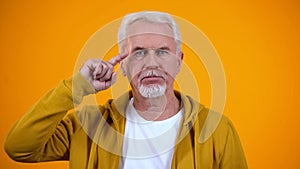 Serious retired male showing screw loose sign on camera, nonsense or absurd