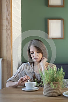 Serious sad irritated woman in cafe with cup of latte coffee. Middle-aged woman sits at a table in cafe. Vertical frame