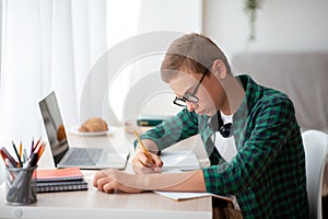 Serious schooler doing homework at his room, writing in notebook