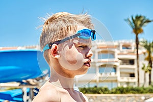 Serious schooler with goggles stands against hotel building