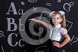Serious schoolgirl standing before the chalkboard as a background pointing the hand into the chalkboard. Landscape