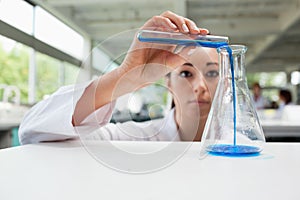 Serious science student pouring liquid