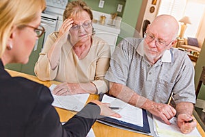 Serious Senior Adult Couple Going Over Documents in Their Home with Agent At Signing