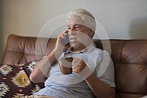 Serious senior aged man doing phone call sitting at home with smart phone - sad emotion elderly people lonely indoor - caucasian