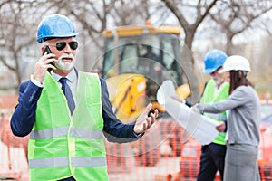 Serious senior architect or businessman talking on the phone while working on a construction site