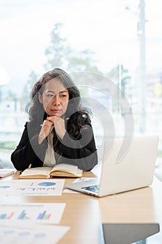 A serious senior Asian businesswoman looking at her laptop screen with a thoughtful, serious face