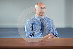 Serious senior businessman sits behind empty desk