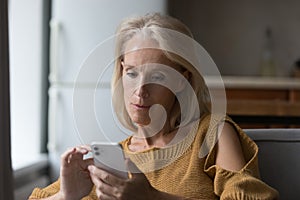 Serious senior elder lady using online app on smartphone