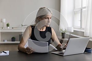 Serious senior freelance business woman checking paper invoice